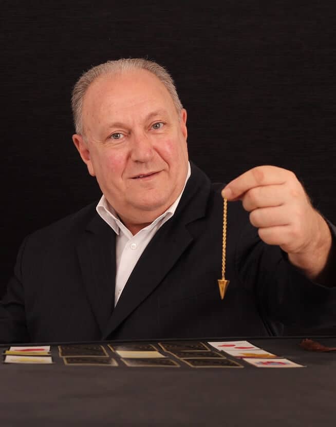 Kinen voyant meduim Homme mature tient dans sa main un pendule divinatoire devant un tirage de carte du tarot pendant une consultation de voyance