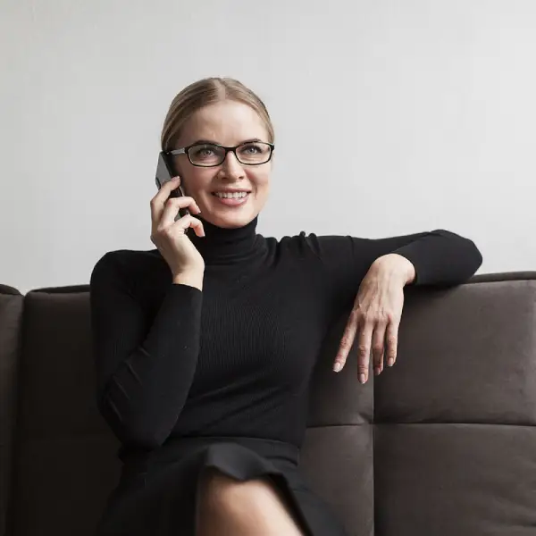 Voyance par téléphone de qualité Femme mature moderne souriante assise dans un salon téléphone à la main pendant une consultation de voyance par téléphone en ligne avec le cabinet de kinen voyant médium